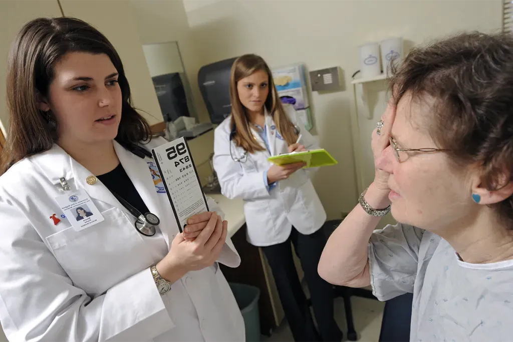 Two C O M students test a geriatric patient's eyesight in an examination room