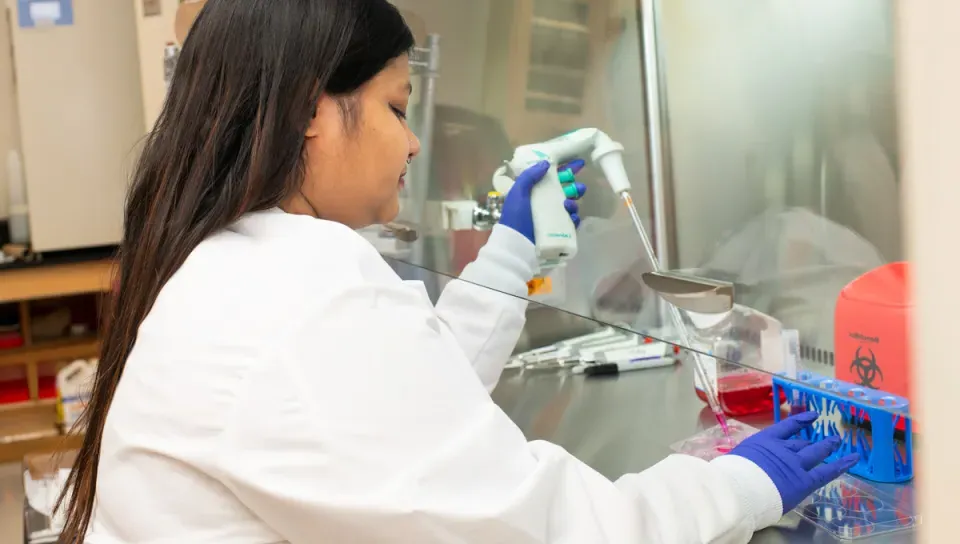 A student in a white lab coat prepares liquids into a tube